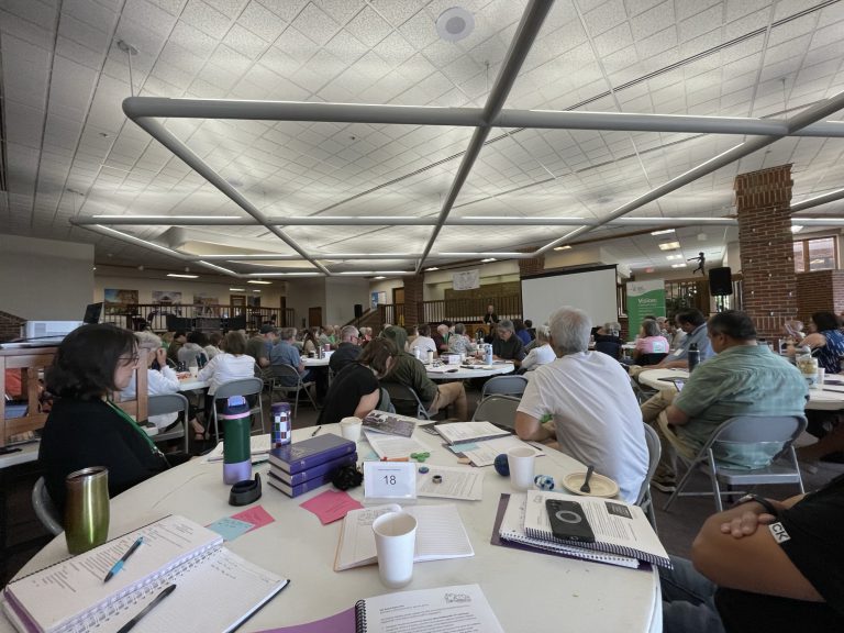 Conference attendees seated at round tables with notebooks and papers during a Central District Conference session.